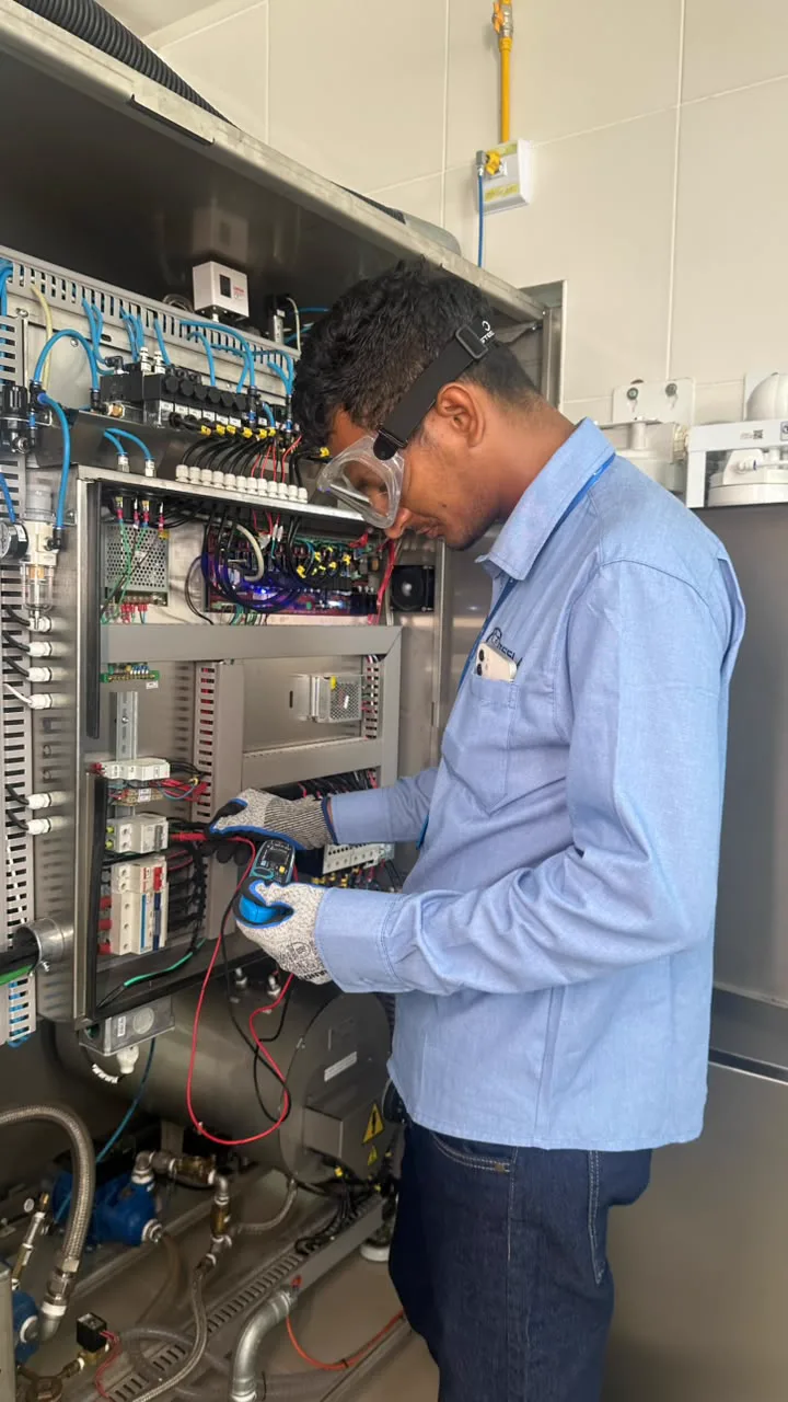 Técnico da Tesla medindo o painel elétrico de um equipamento, de óculos de proteção e luvas